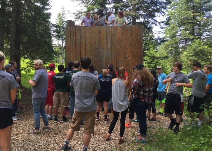 Image of a young adult group navigating the wall-climbing portion of the ropes course/obstacle course area at Camp Wittman Outdoor Center